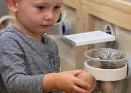 A child engaged in a practical life activity, carefully transferring water with a sponge.